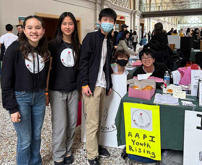 Five teens pose next to a table with a sign reading AAPI Youth Rising.