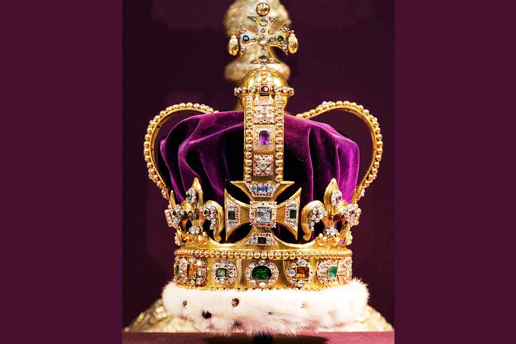 A gold crown with many jewels and purple velvet sits on a surface.
