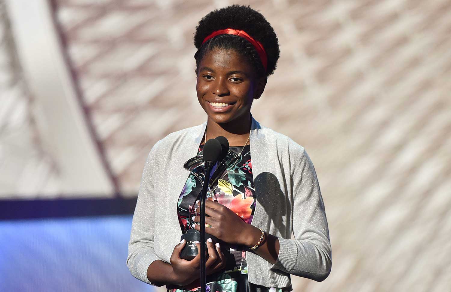 Zaila Avant-garde smiles and holds a trophy at a microphone.