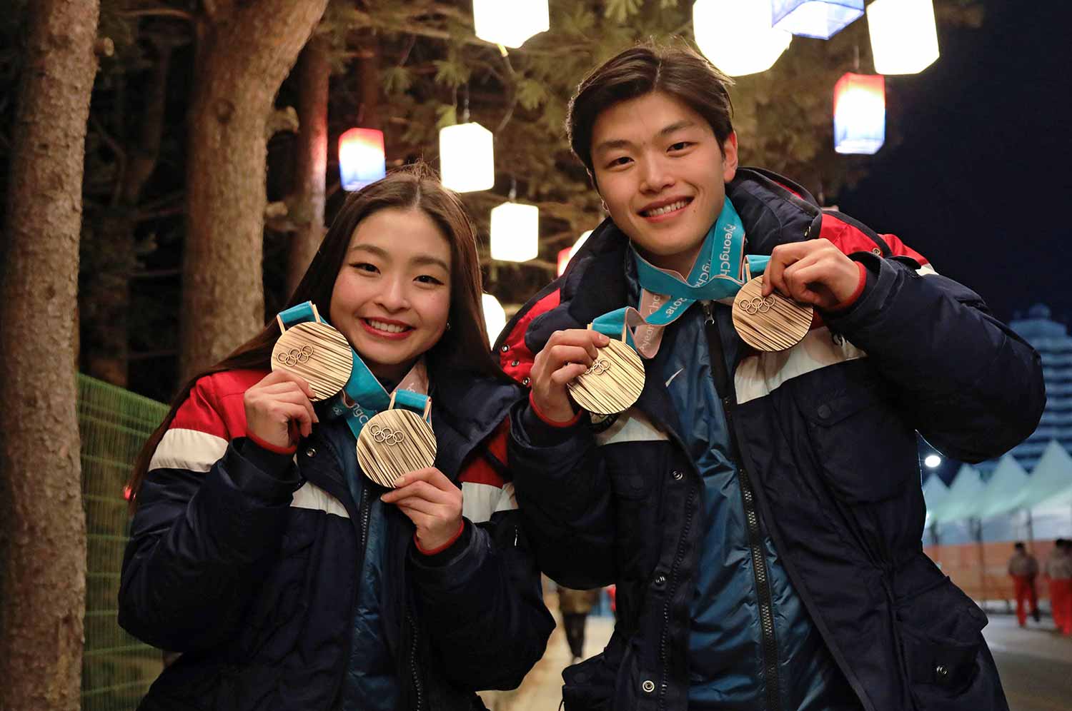 A young woman and a young man smile and hold up two Olympic medals each.