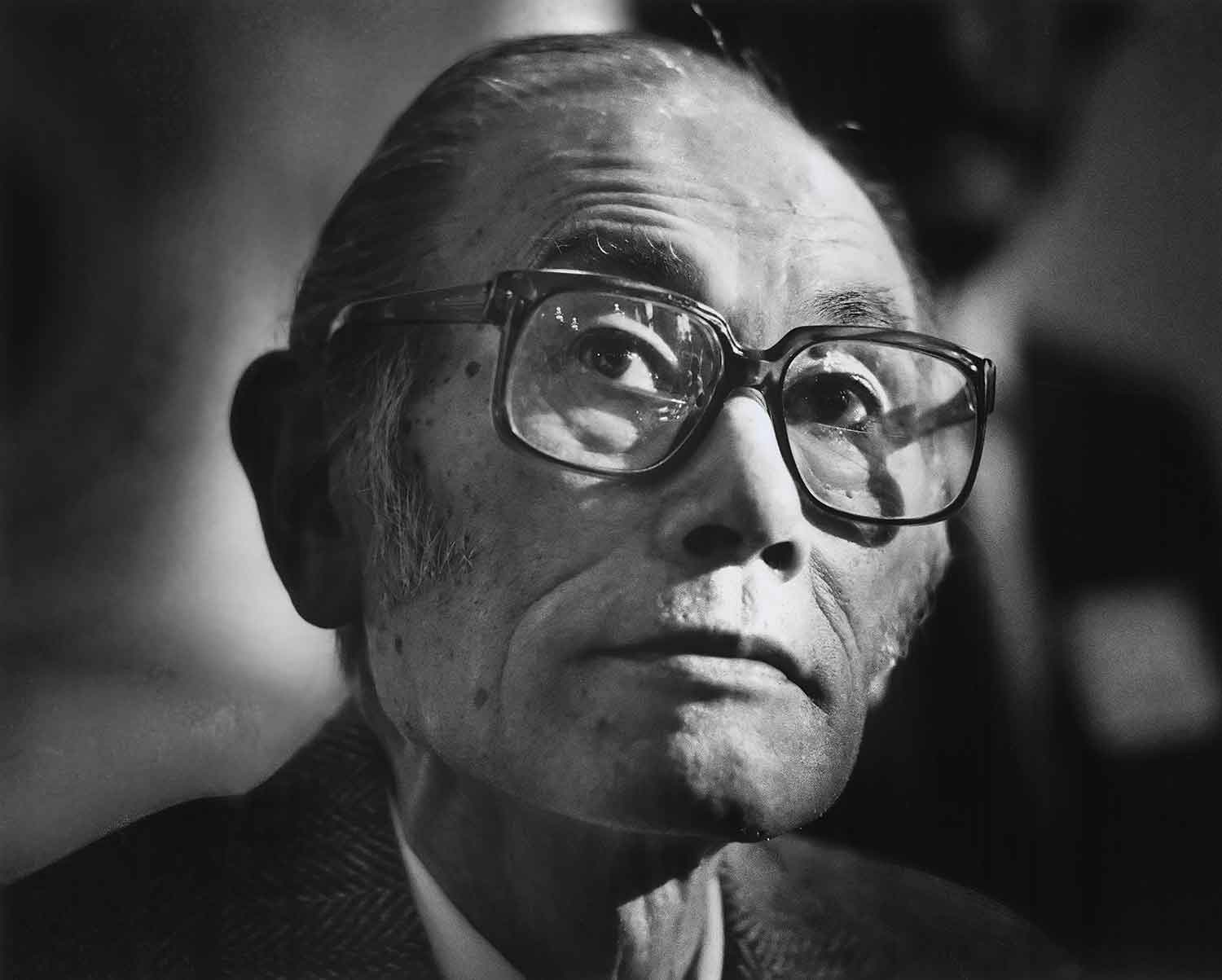 Black and white portrait of a man wearing a jacket and glasses.