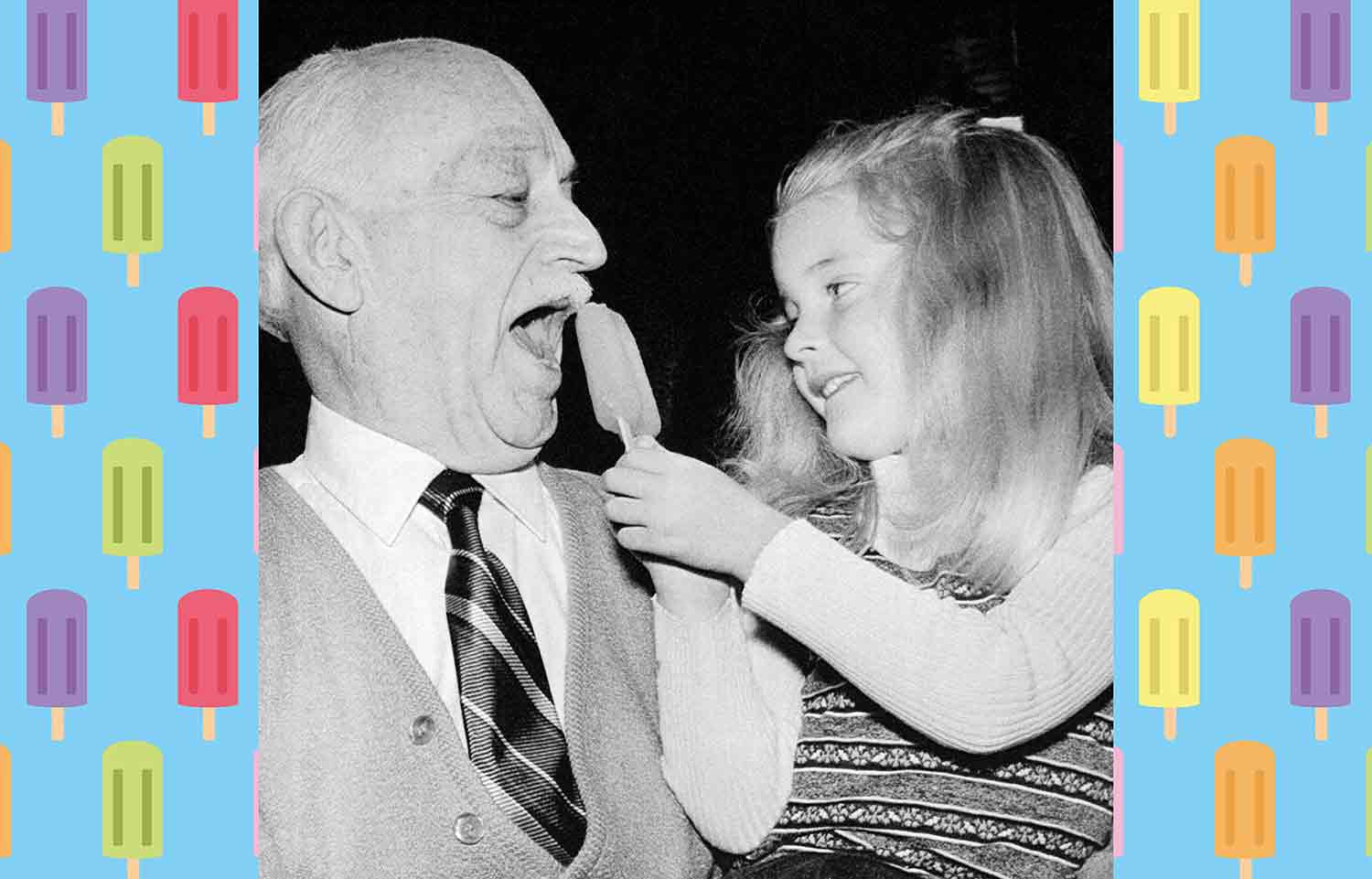 A man holds a young girl who holds a popsicle.