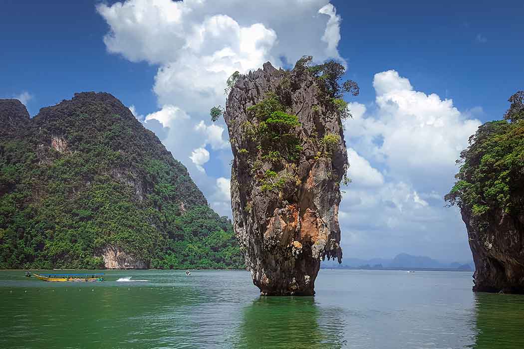 A rock formation juts out of a body of water with cliffs in the background.
