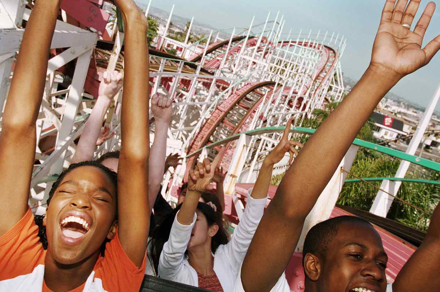 Teens ride a roller coaster with their arms raised.