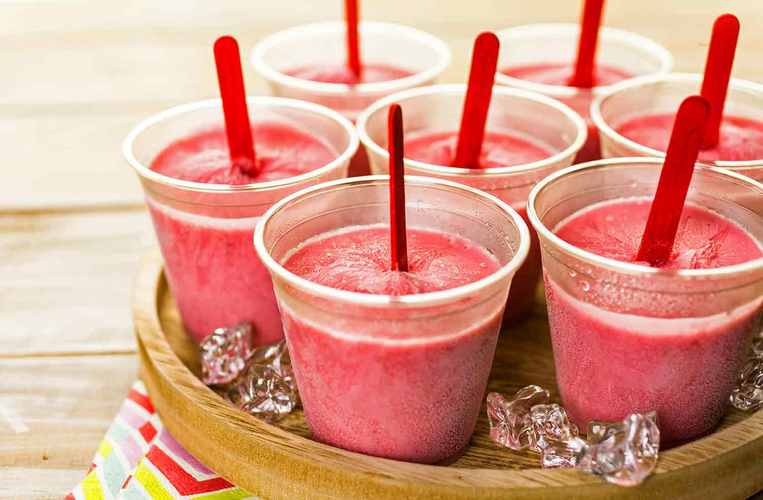 Pink frozen substance in plastic cups, each with a stick.