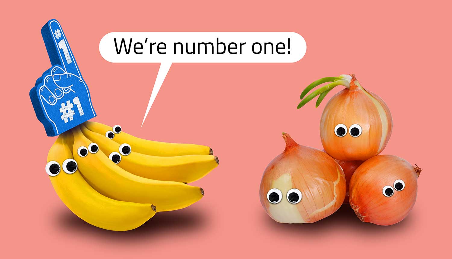 A bunch of bananas with googly eyes wears a number 1 foam finger and says we’re number one to a group of onions with googly eyes.