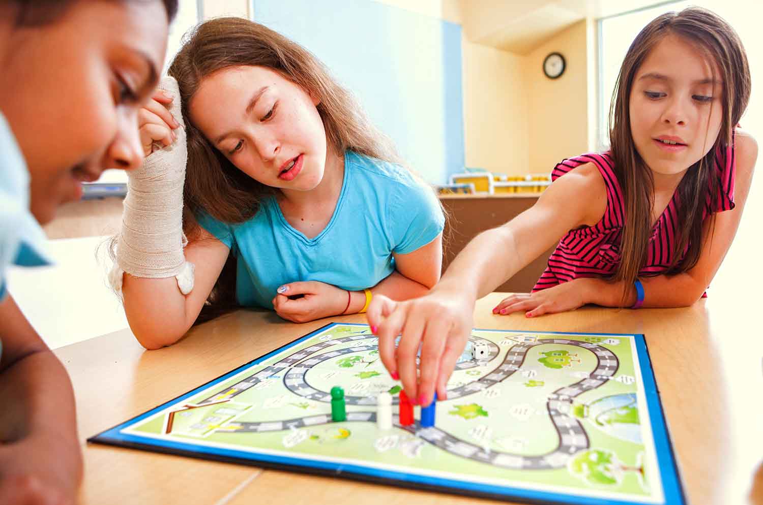 Three elementary school kids sit at a table playing a board game.