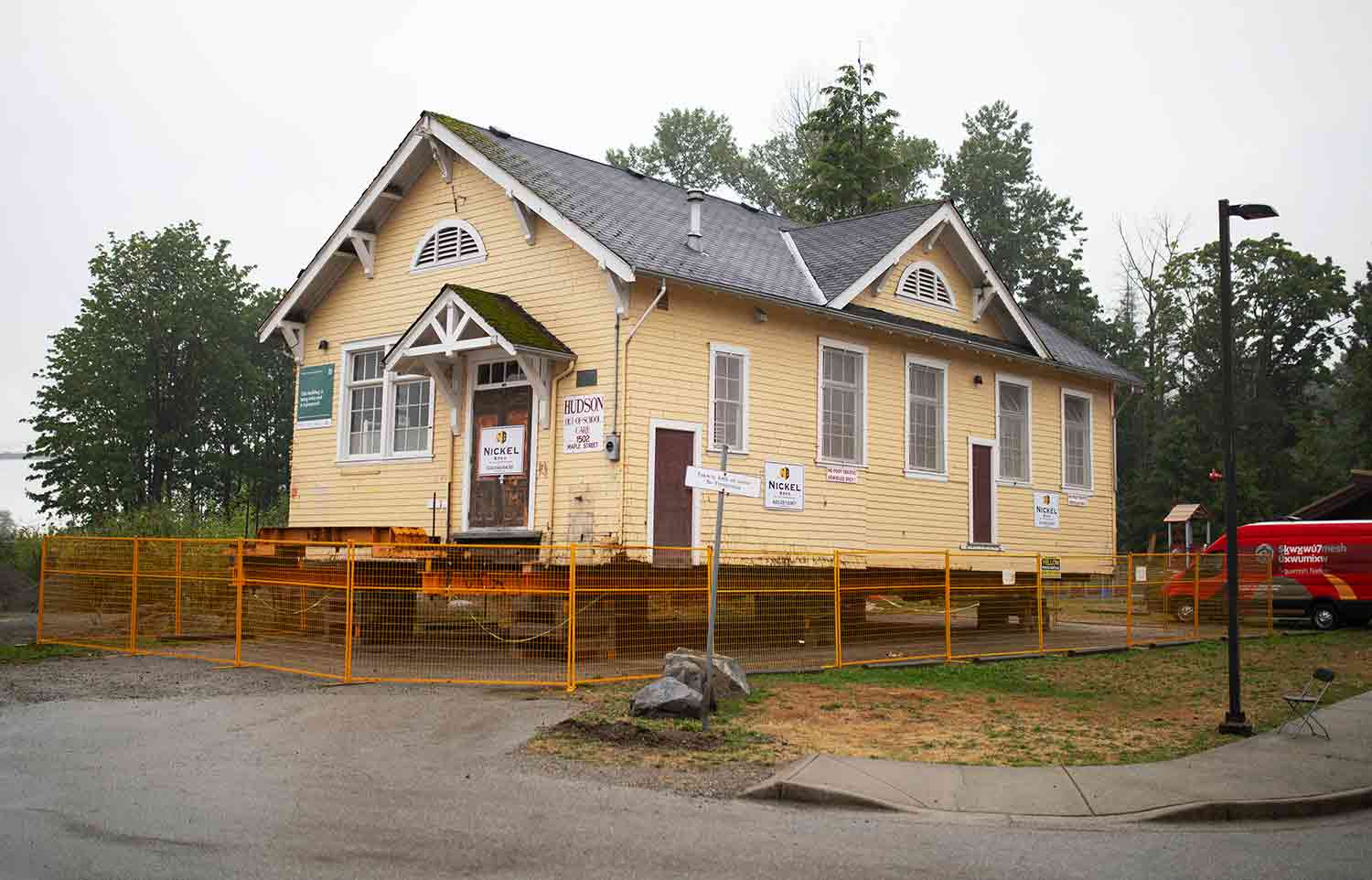 A small yellow school building sits on cement blocks and is surrounded by an orange fence.