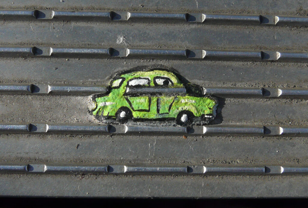 A green painting of a car on a lumpy background pressed into an outdoor grate.