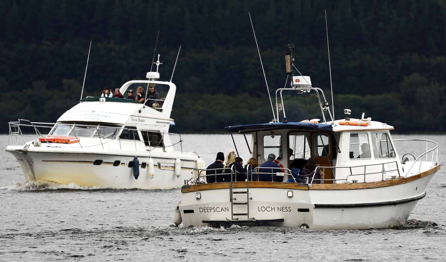 People aboard a boat called Nessie Hunter and a boat called Deep Scan Loch Ness on a body of water.