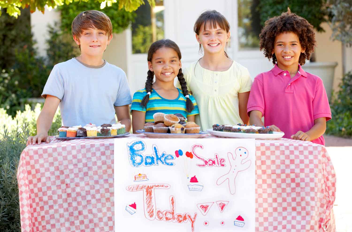 Four children pose behind a take with baked goods and a sign that says Bake Sale.
