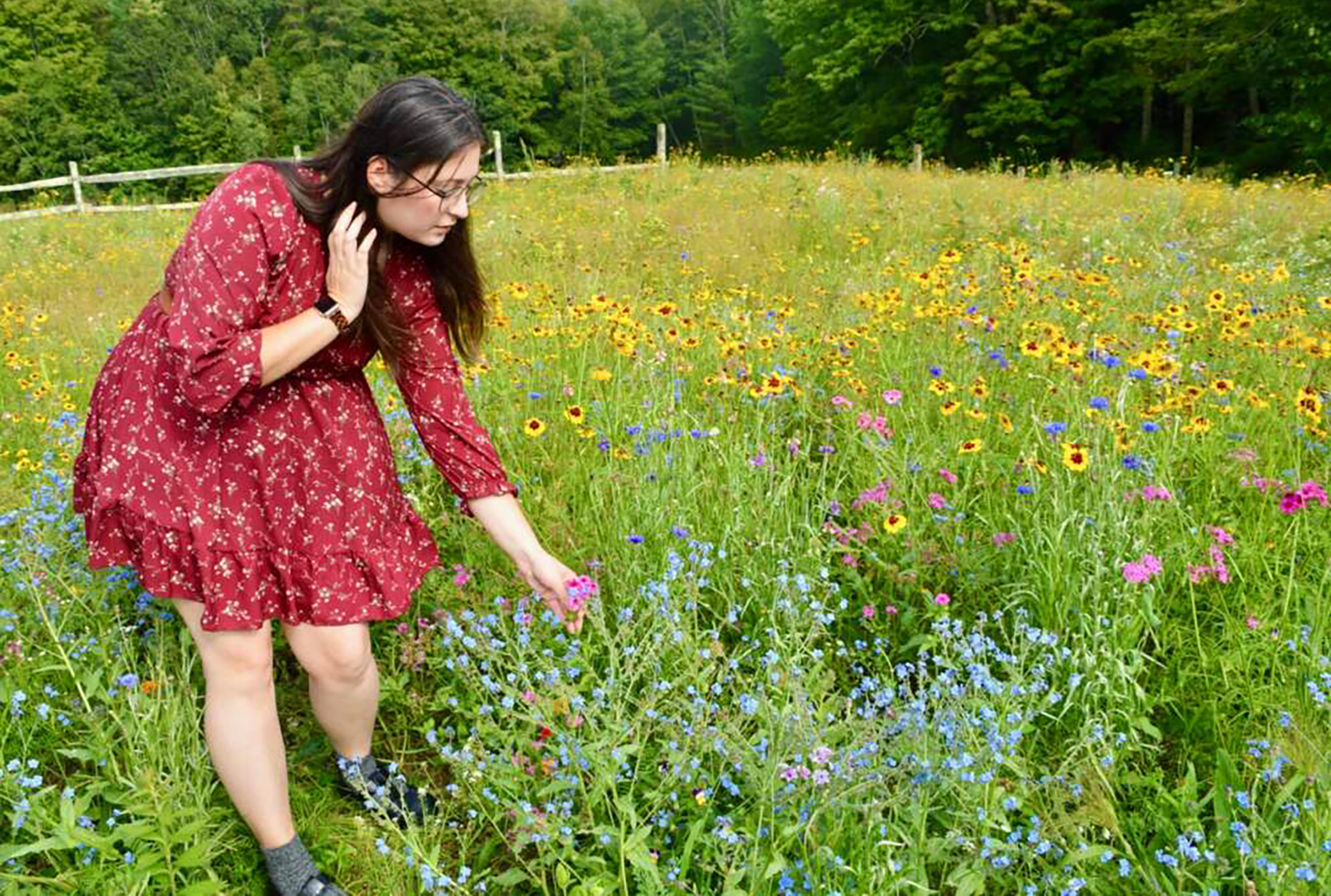 A woman stands in a field of wildflowers and leans over to touch one of the flowers.