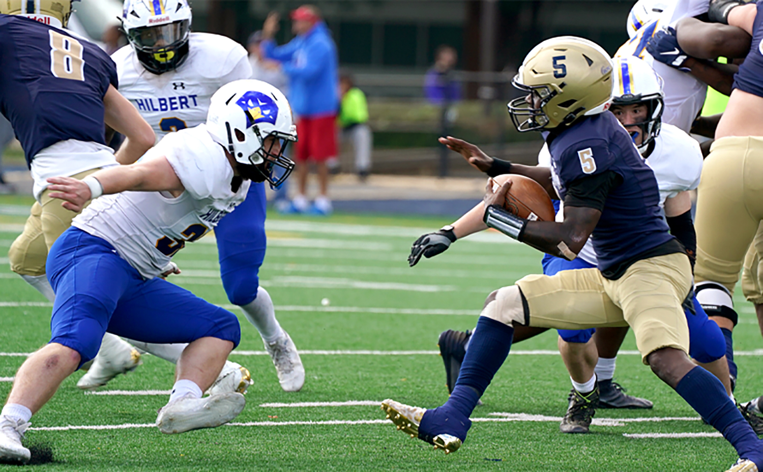 A football player holding a football faces off with an opposing player on a field.