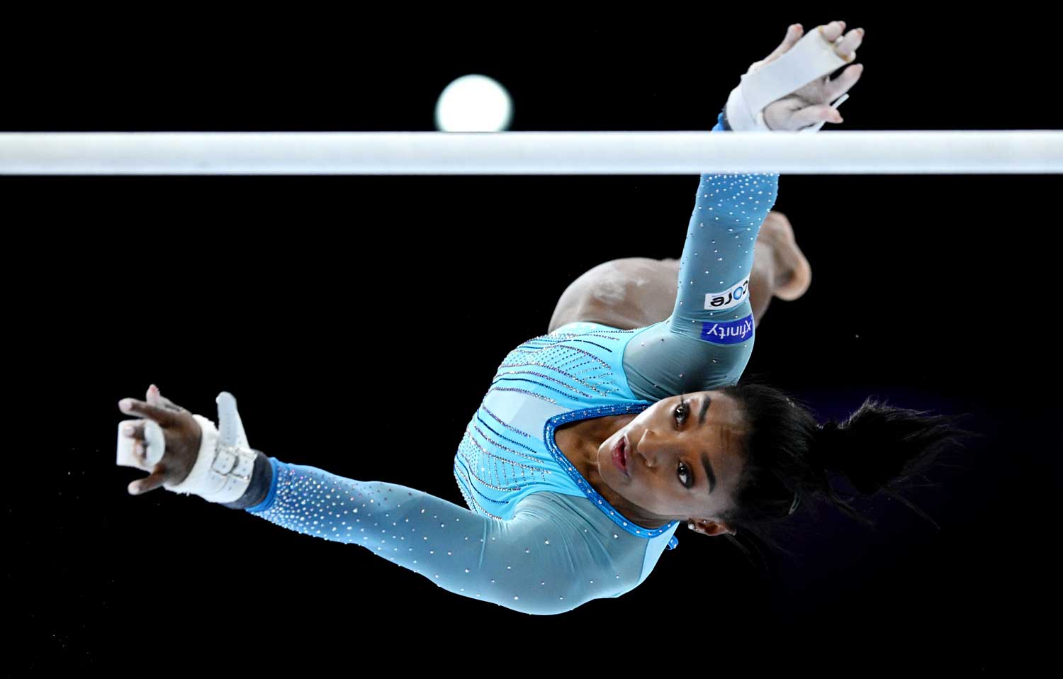 Simone Biles is horizontal in midair as she reaches for one of the uneven bars.