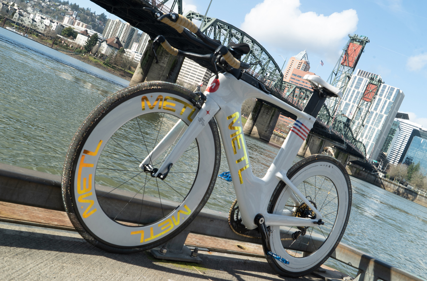 A white bicycle with shape memory tires leans against a bridge railing.