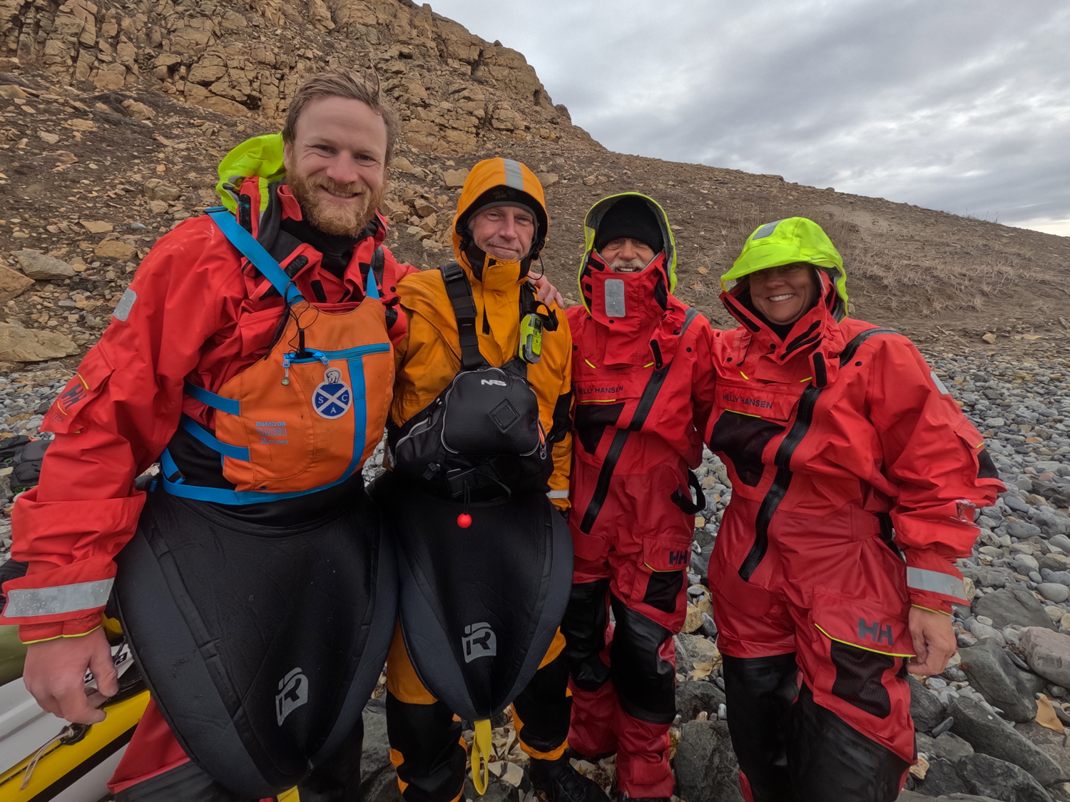 Three men and one woman in head to toe red and orange gear pose on a rocky landscape.