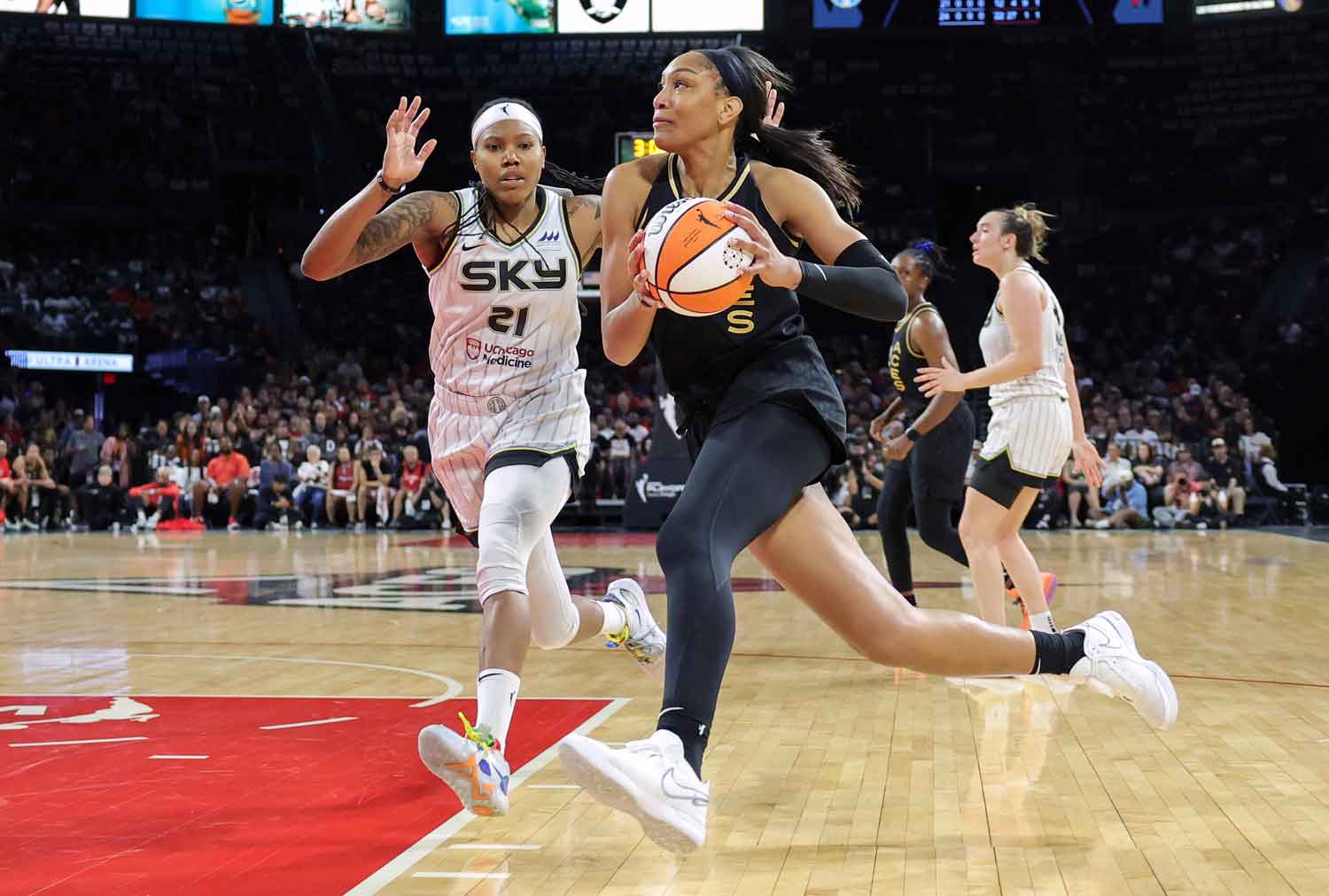 A’ja Wilson holds the ball and runs as another player tries to block her.