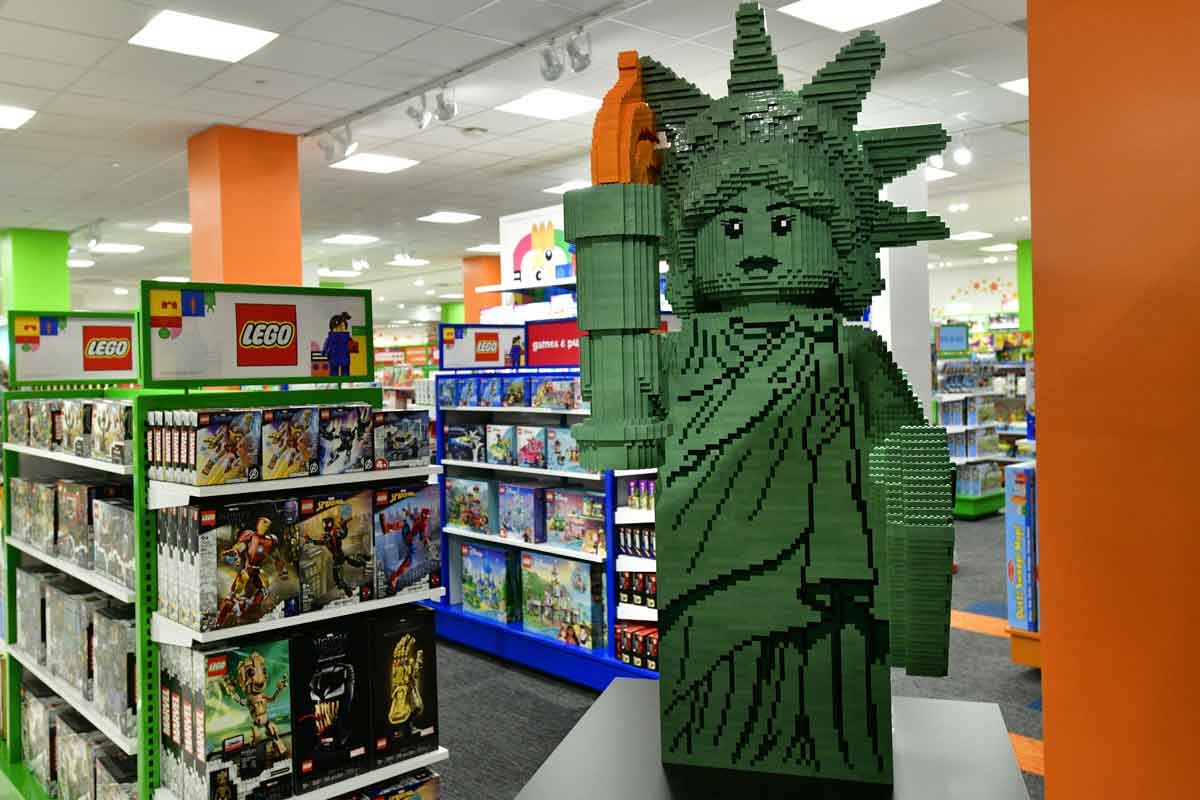 A large LEGO Statue of Liberty is next to the LEGO section of a Toys R Us store.