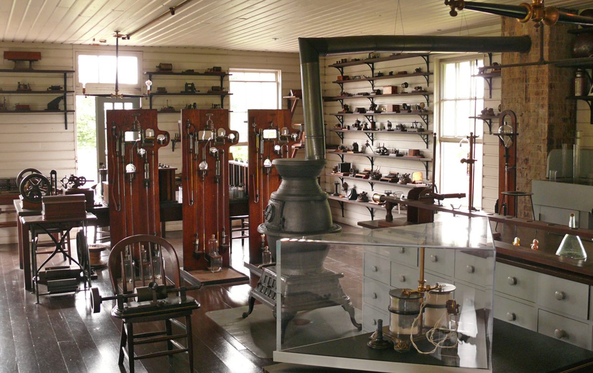 A potbelly stove sits in the center of a room full of 19th century scientific equipment as well as chairs and storage spaces.