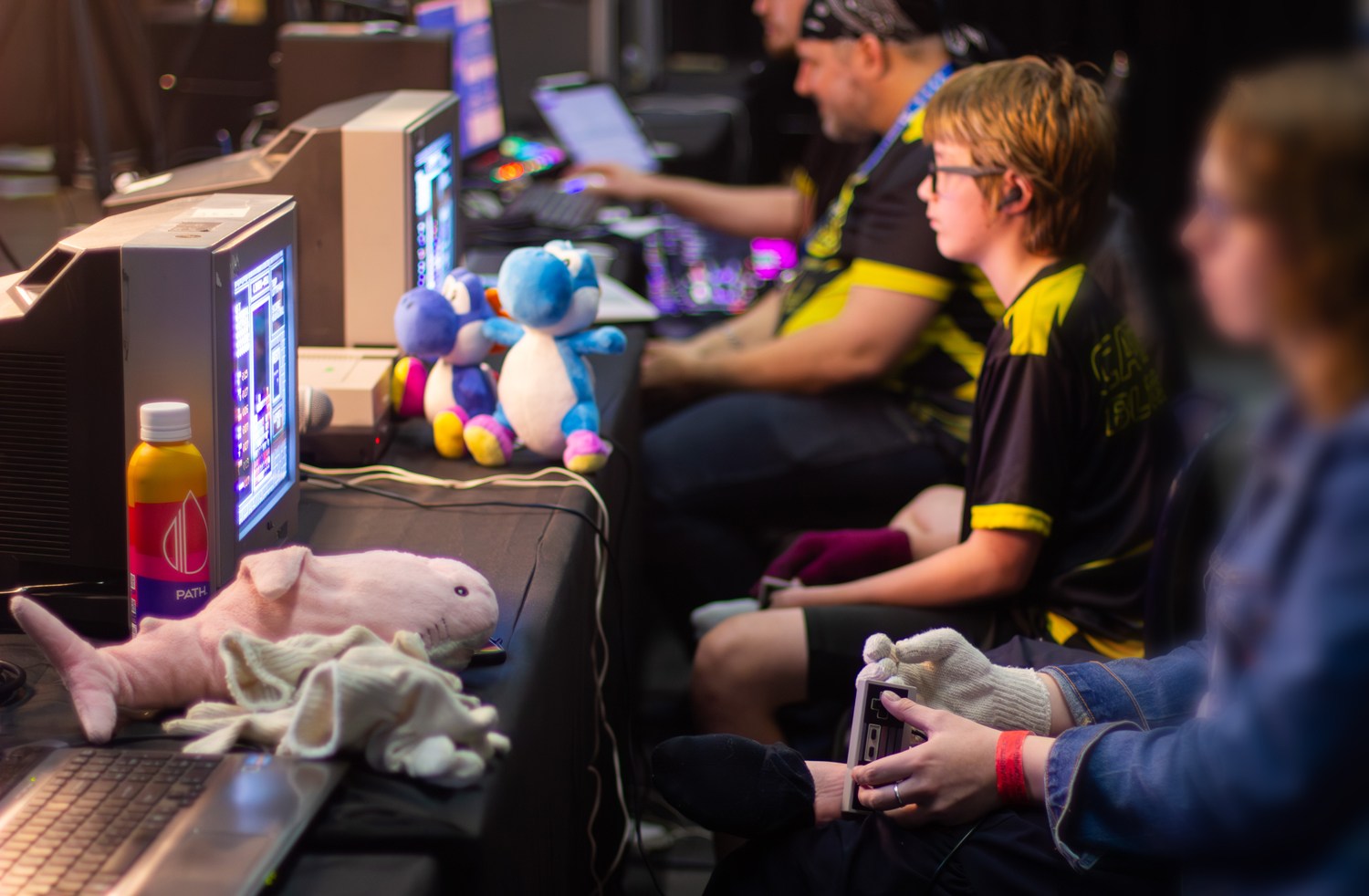 A row of men and teens sit in front of screens holding game controllers and playing Tetris.