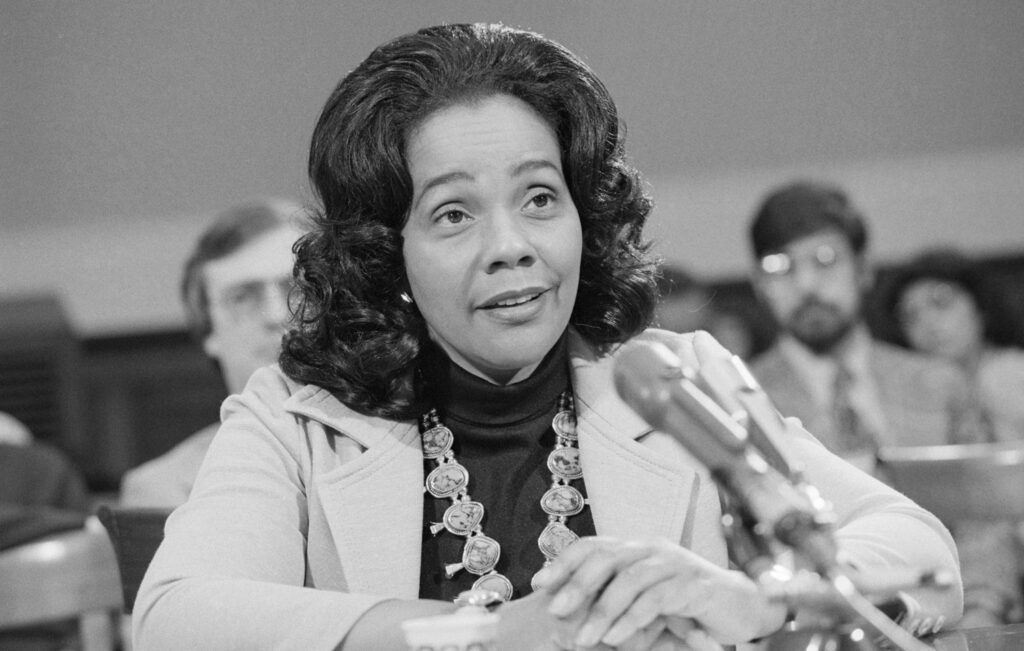 Black and white photo of Coretta Scott King seated behind a microphone.