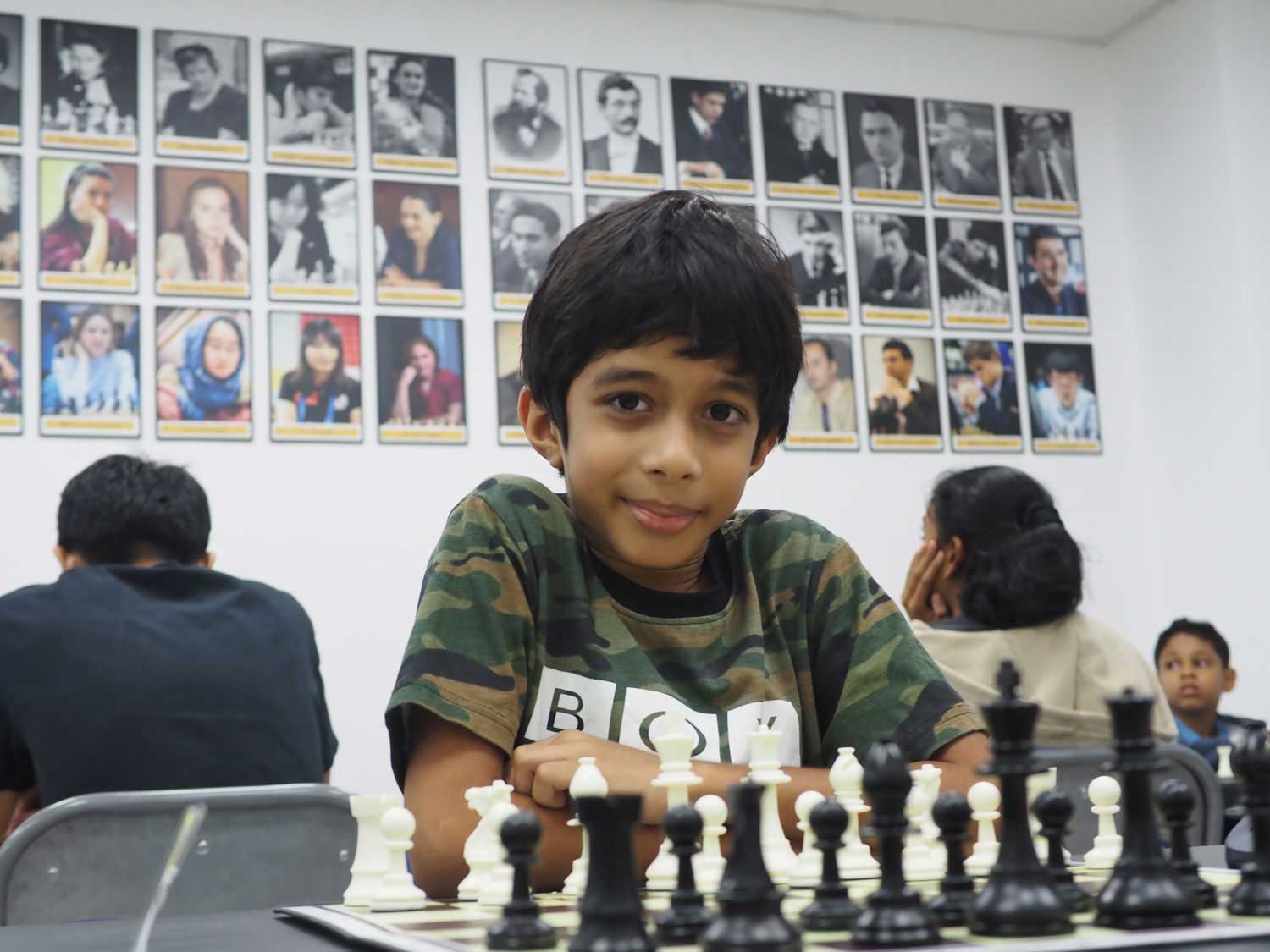 A young boy sits behind a chess board that has been set up for a game.