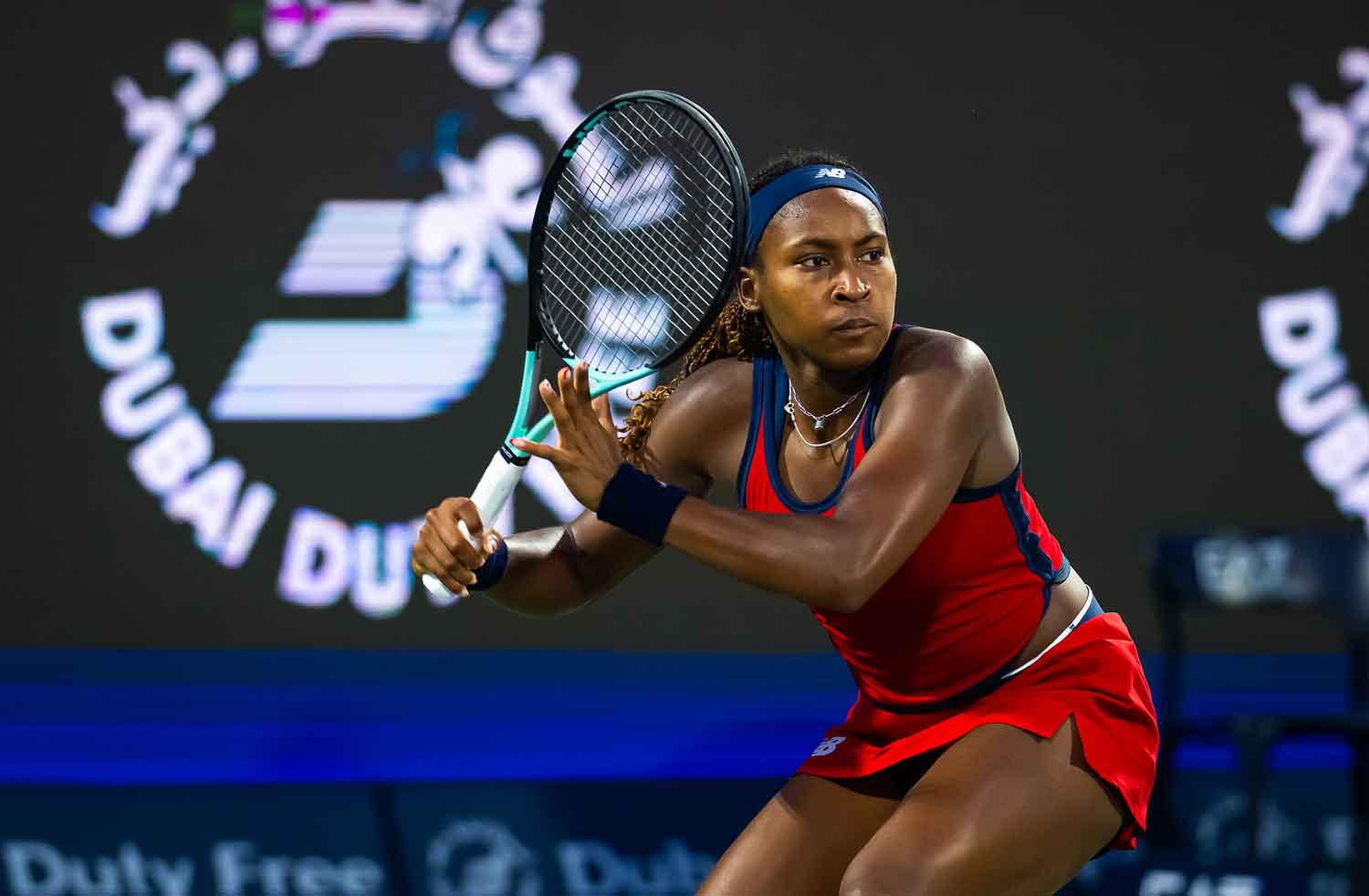 Coco Gauff stands on a tennis court holding up a racket and poised to hit a ball.