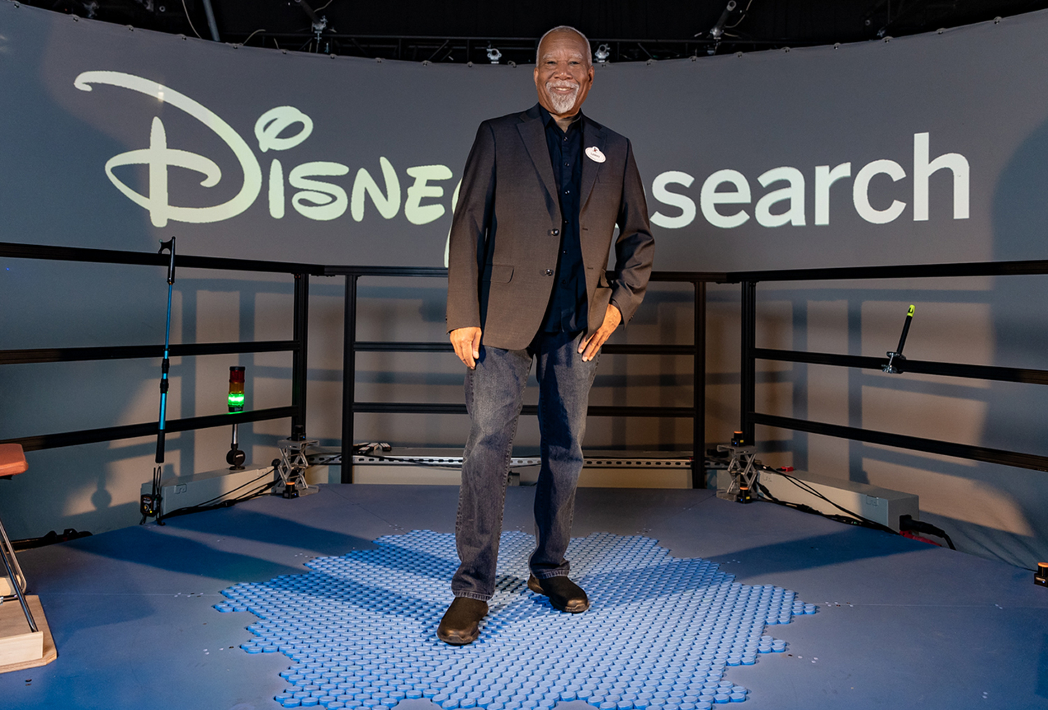 Lanny Smoot stands on a platform in front of a sign reading Disney Research.