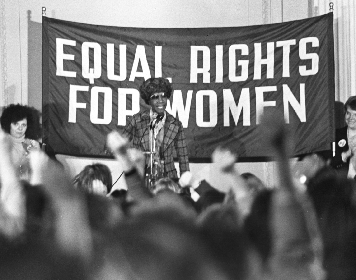 Shirley Chisholm speaks before a crowd and stands in front of the sign that reads equal rights for women.