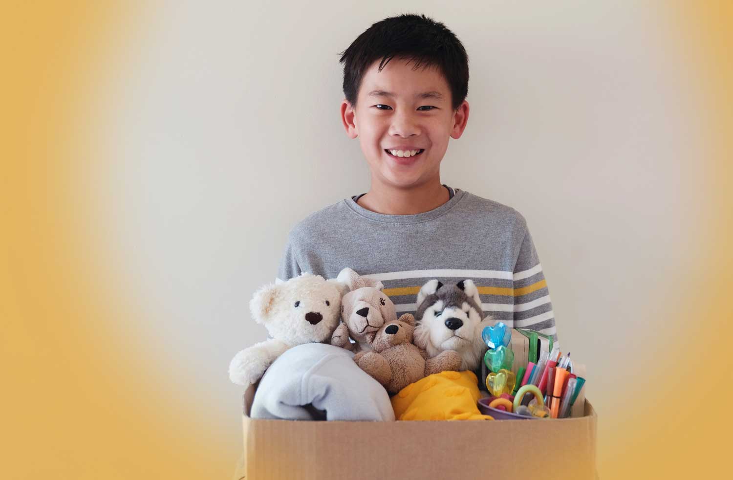 A child holds a cardboard box full of toys.