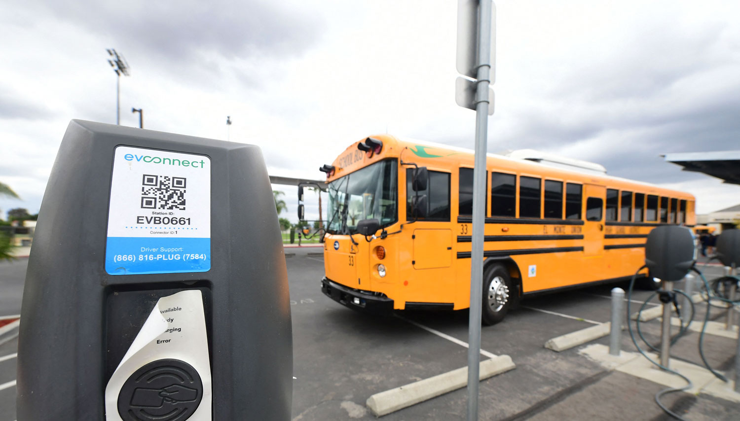 An electric school bus is parked in a parking lot next to an electric charging station.