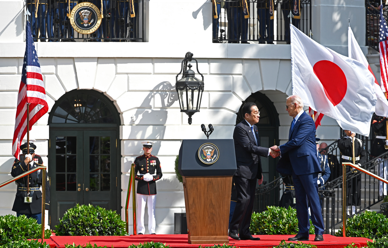 President Joe Biden and Japanese Prime Minister Fumio Kishida shake hands in front of the White House and are flanked by the U.S. and Japanese flags.
