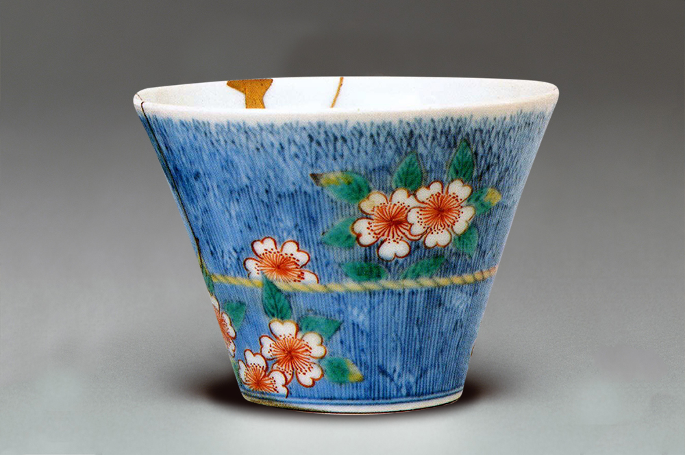 Cherry blossoms are painted on a blue background on the outside of a cup.