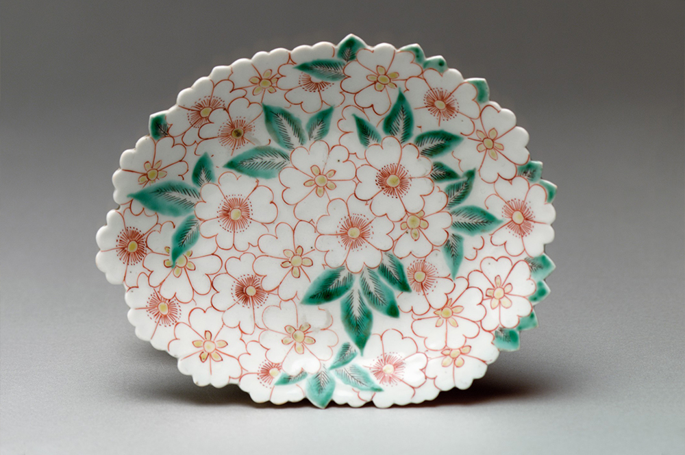 Pink, yellow, and white cherry blossoms and green leaves decorate a dish.