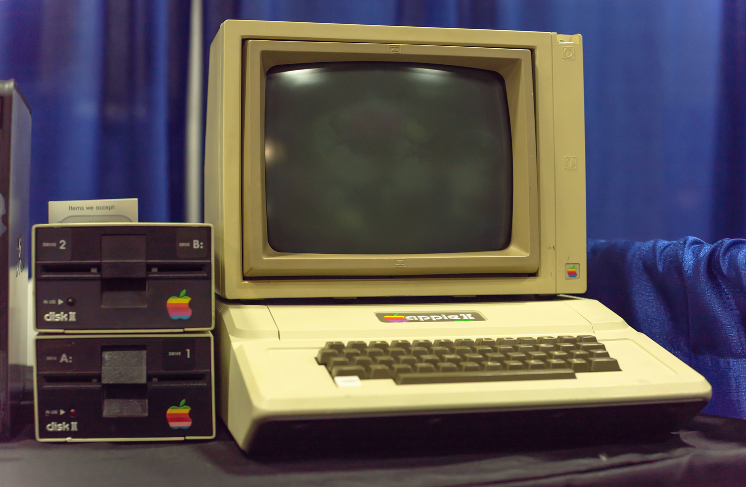 An Apple II computer sits on a desk next to two floppy disk drives.