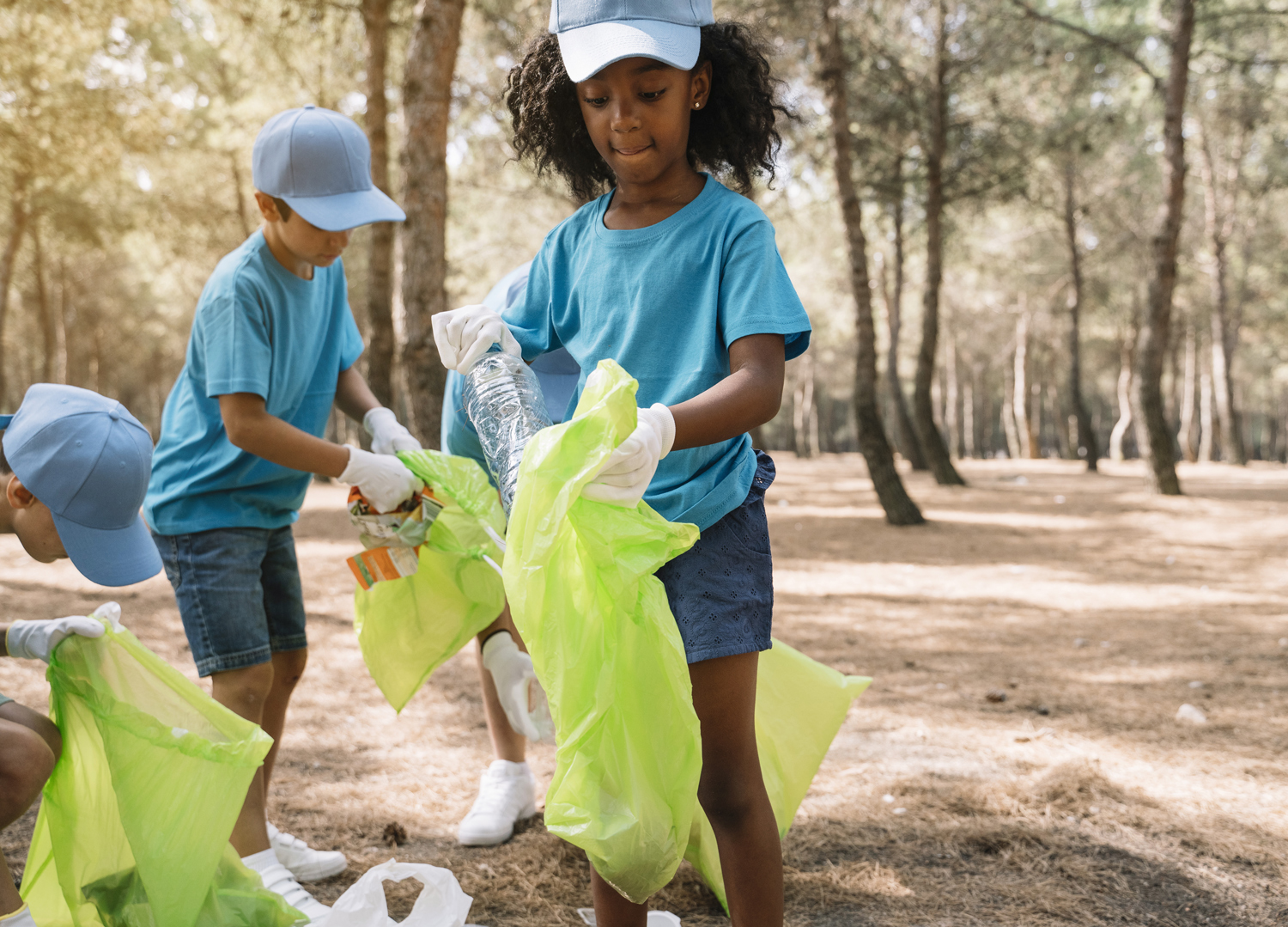 Young children in a wooded area put litter into plastic bags.