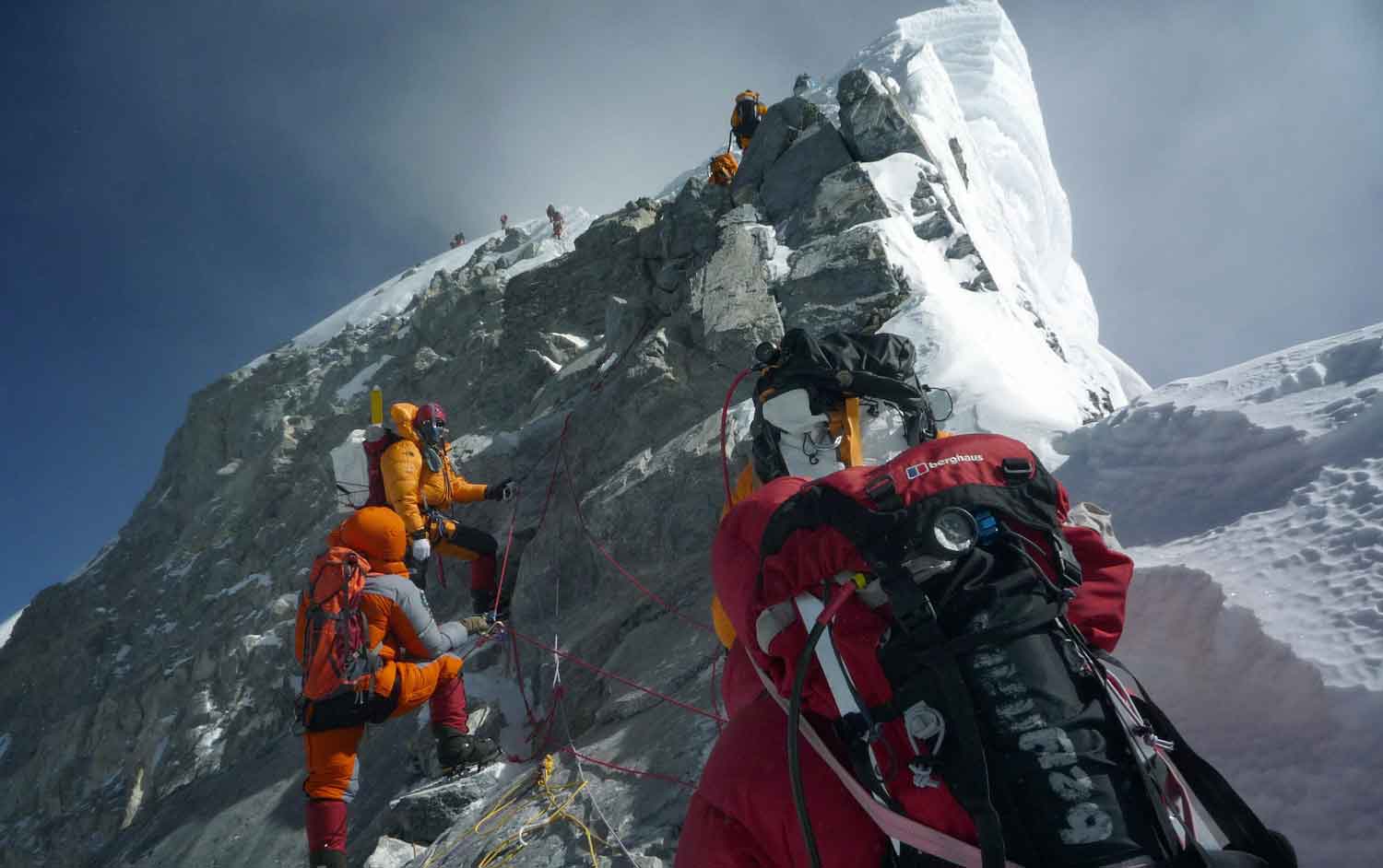 A group of climbers with oxygen tanks and other gear approach the summit of Mount Everest.