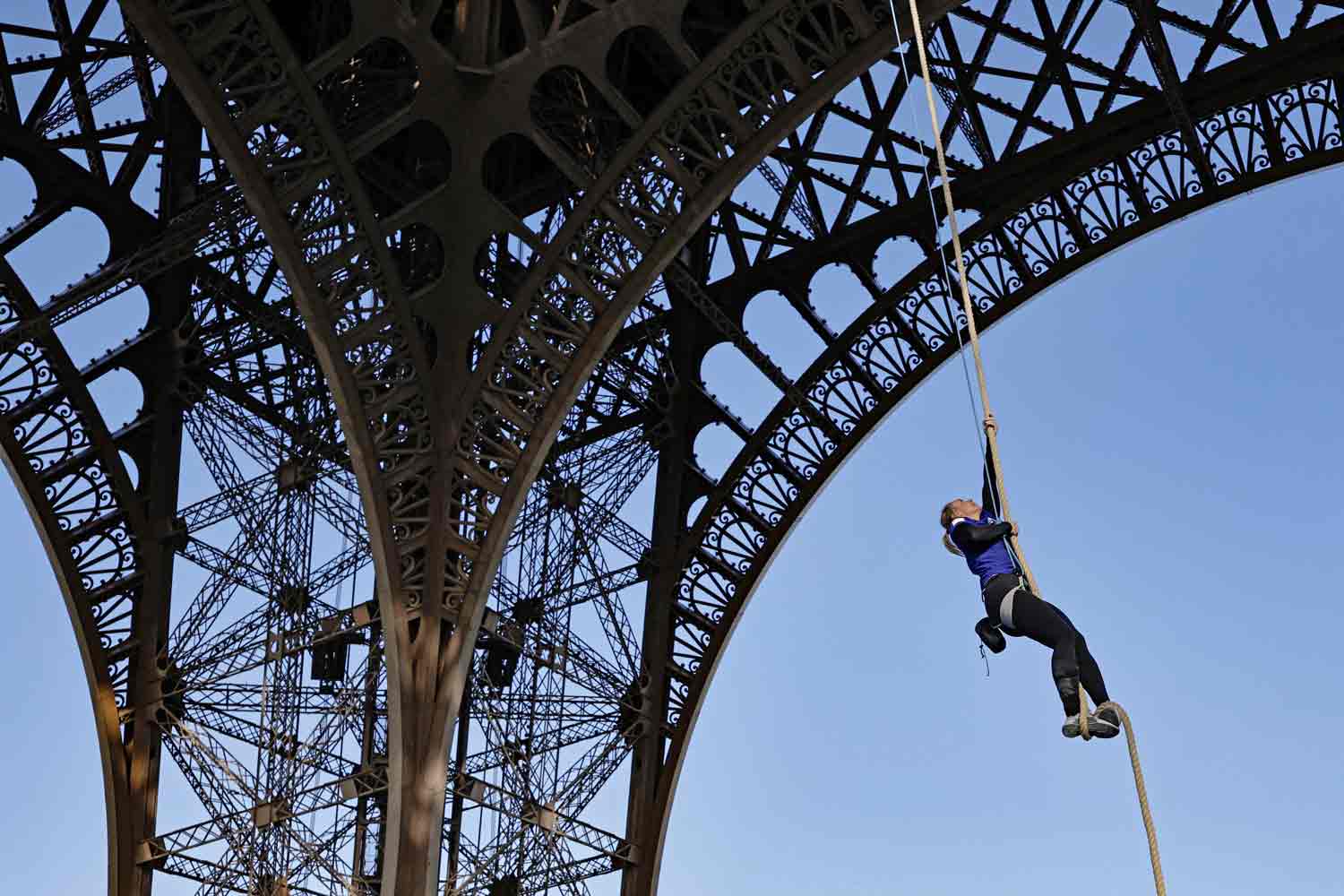 A woman climbs a rope that is hanging from the Eiffel Tower.