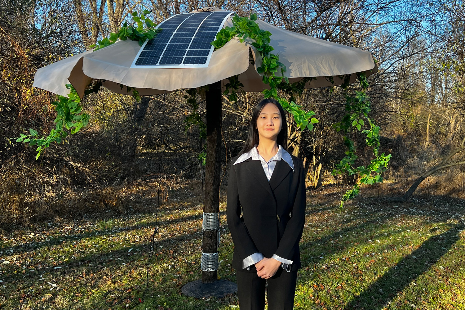 A teen stands in front of a patio umbrella to which solar panels and wire mesh have been added.