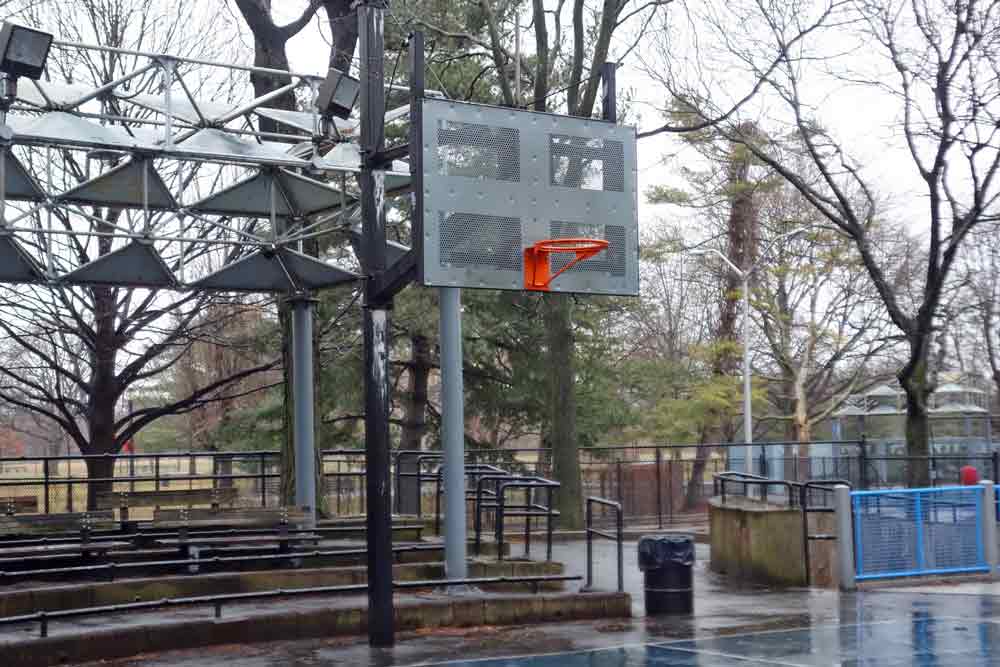 A low-mounted basketball hoop on an outdoor court with a seating area behind it.