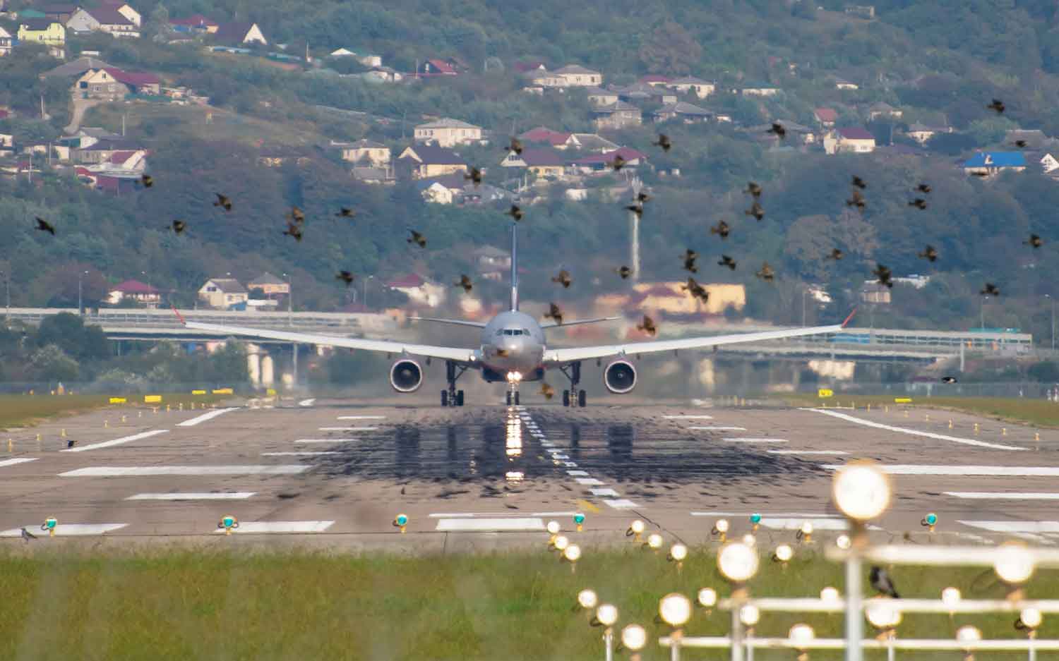 An airplane sits on a runway with houses in the background.