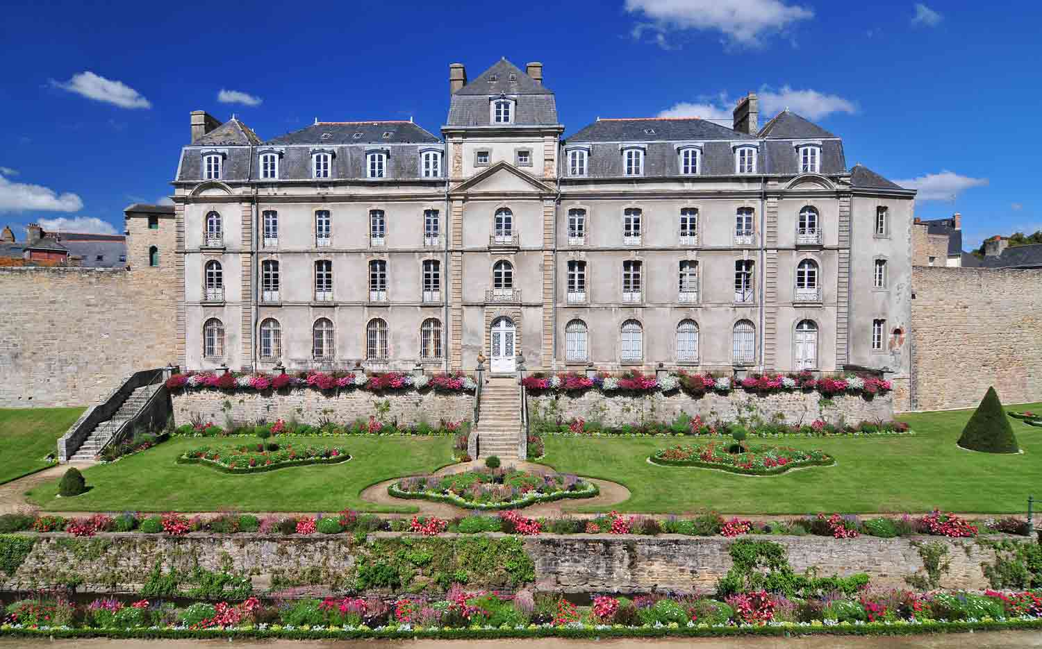 A large 18th century building with a lawn and flowers in front.