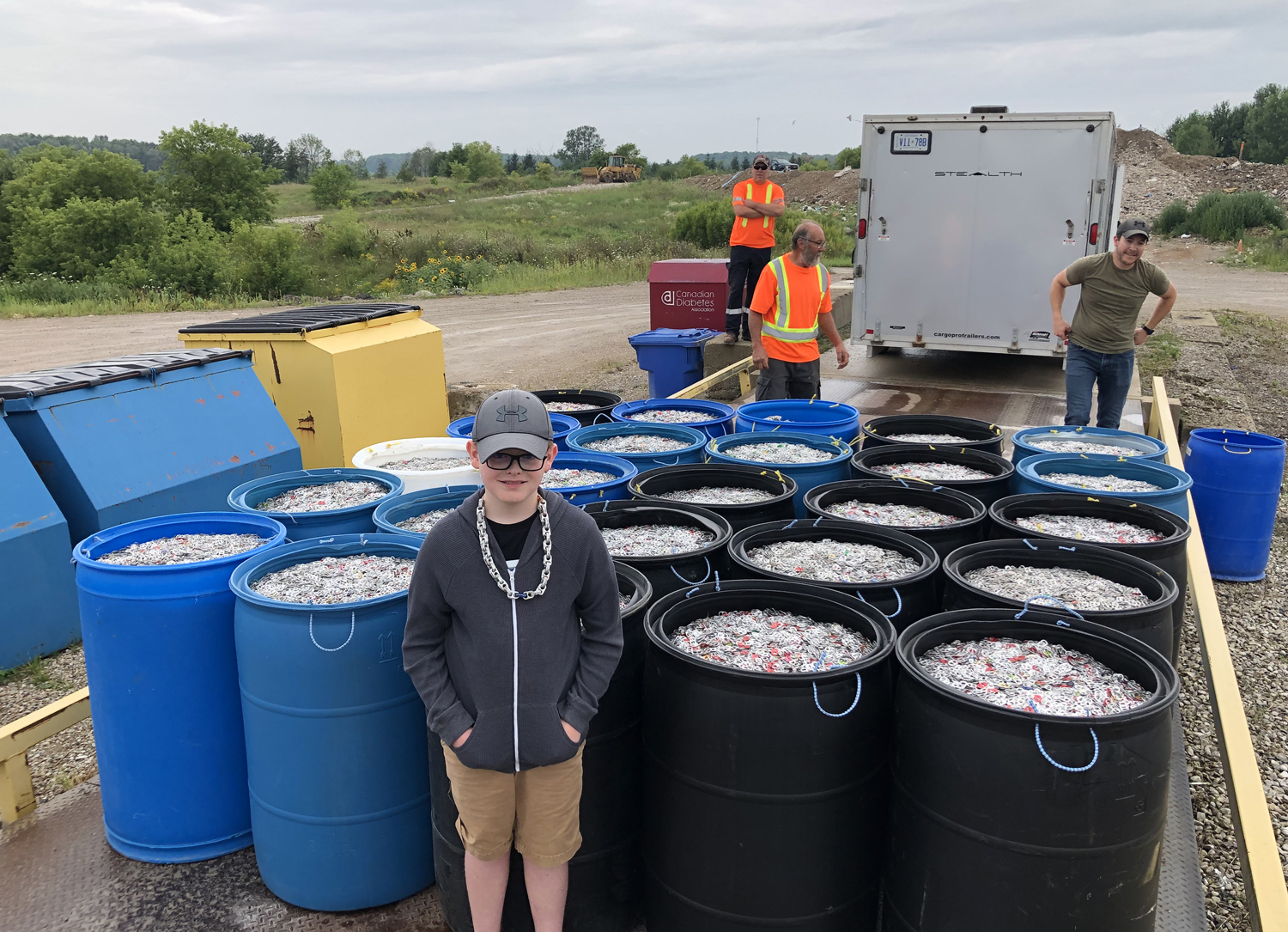 A child poses with 25 tall containers of can tabs.