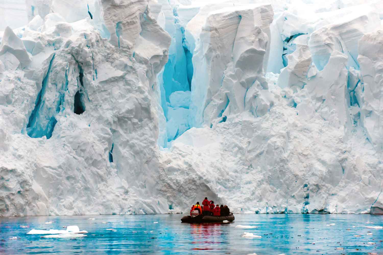 People in an inflatable vessel approach a giant glacier.