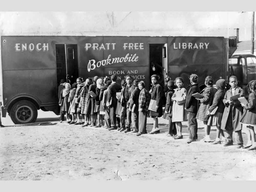 Children line up in front of a bus that says Enoch Pratt Free Library Bookmobile.