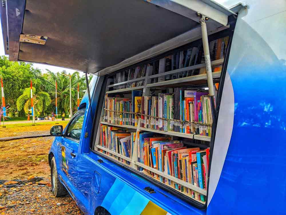 An open door on the side of a blue vehicle reveals that there are bookshelves built into the van.