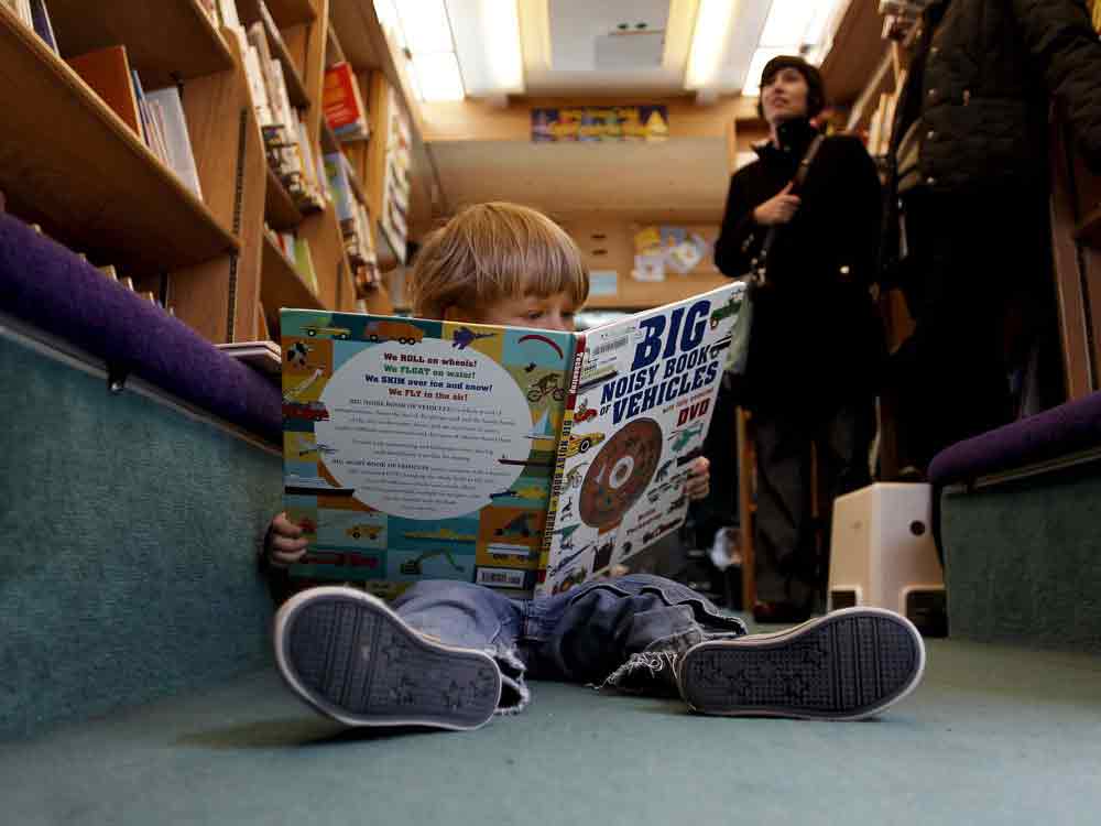 A small child looks at a large book on the floor of the interior of a bookmobile.