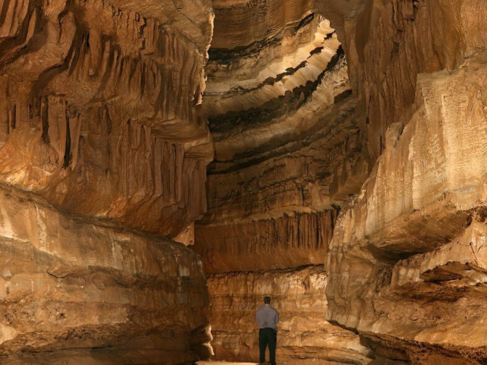 A man stands in a limestone formation with a ceiling that is well over 100 feet high.