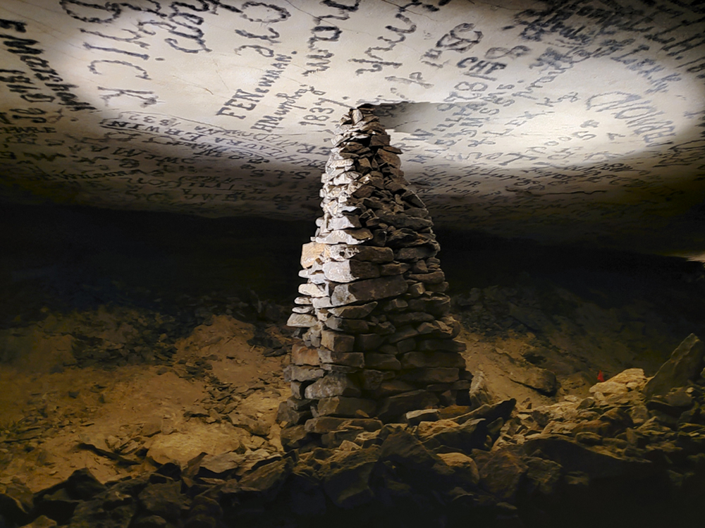 A large monument of rocks sits under a cave ceiling that is covered in writing.