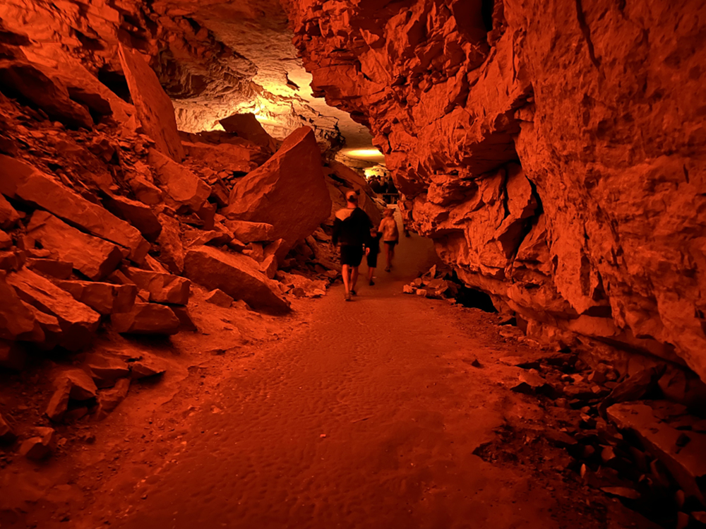 Two adults and a child walk through a cave corridor that appears to be tinted red.